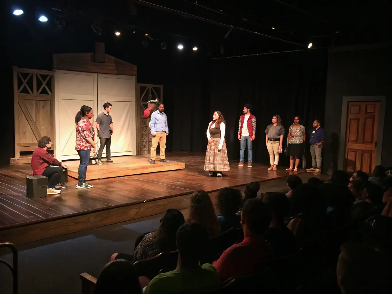 A photograph capturing a live theater performance in a community center, showcasing actors on stage and an engaged audience.